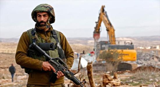  Un soldado israelí vigila mientras una excavadora demuele una casa palestina en una aldea en la Cisjordania ocupada, 16 de enero de 2020. (Foto: AFP)